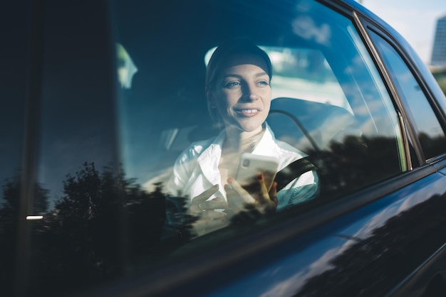 vrolijke vrouwelijke ondernemer die naar het raam kijkt en lacht tijdens autorit om naar de vergadering te gaan