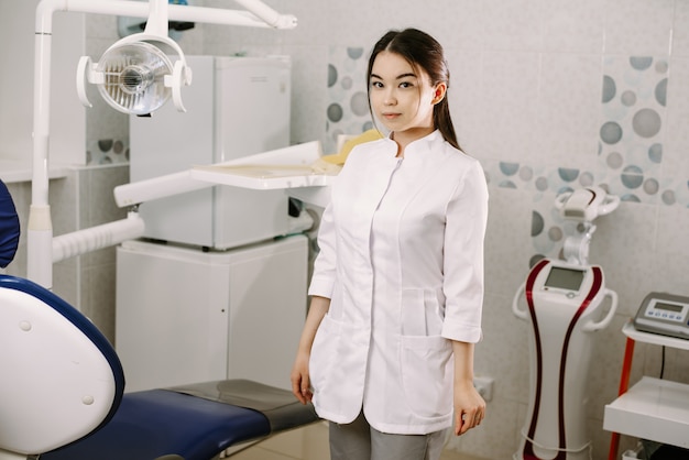 Vrolijke vrouwelijke tandarts die in haar bureau glimlacht. tandheelkunde student permanent in een tandheelkundige behandelkamer