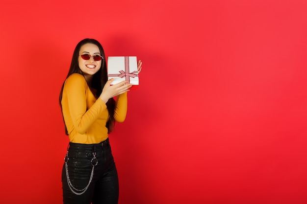 Vrolijke vrouwen gele blouse en rode bril is een witte geschenkdoos met rode strik.