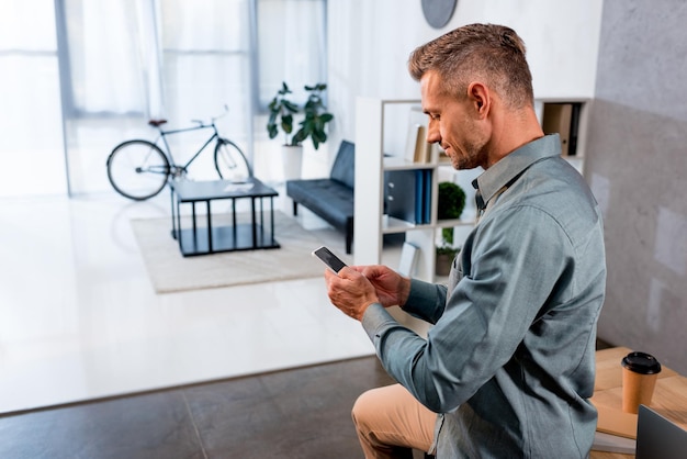 Foto vrolijke zakenman met behulp van smartphone in moderne kantoren