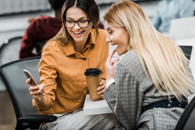 Foto vrolijke zakenvrouwen met een smartphone op het werk in het kantoor