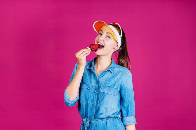 Vrolijke zomerresident brengt aardbeien naar haar lippen. achtergrond roze