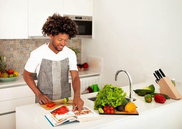 Vrolijke zwarte man die kookboek leest met recepten in de keuken