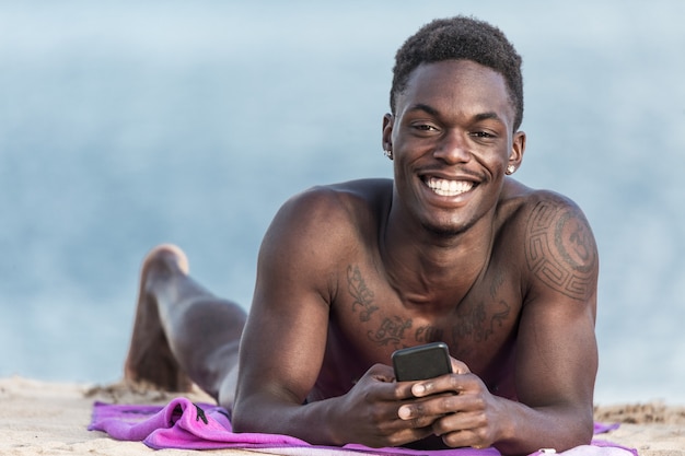 Vrolijke zwarte man met smartphone op strand