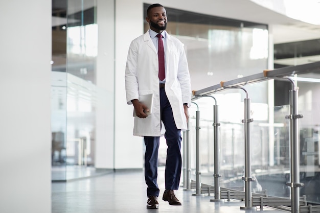 Vrolijke zwarte wetenschapper die door laboratorium loopt met digitale tablet