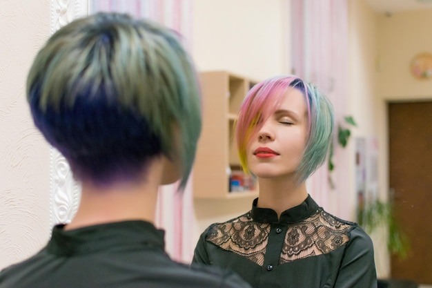 Vrouw 3040 maakte haarkleuring in verschillende kleuren en kijkt in een spiegel in een kapsalon