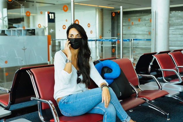 Vrouw aan de telefoon op de luchthaven met beschermend gezichtsmasker tijdens coronavirus.