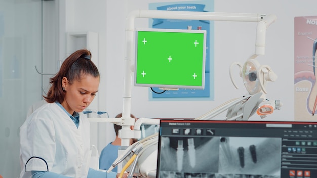 Vrouw aan het werk als tandarts met groen scherm en röntgenscan voor gebitsverzorging in tandheelkundige kast. Mondzorgspecialist die chromasleutel analyseert met geïsoleerde mockup-sjabloon en tandenradiografie