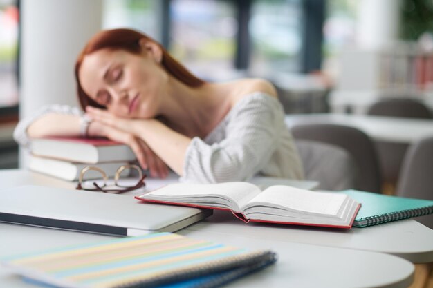 Vrouw aan tafel lag met haar hoofd op boeken in slaap