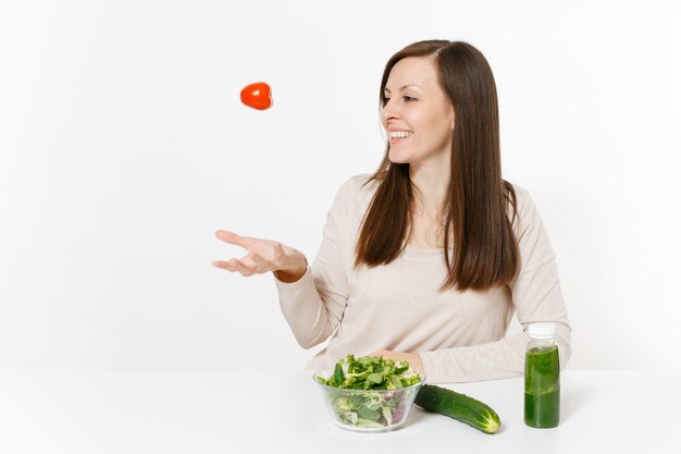 Vrouw aan tafel met groene detox smoothies, frisse salade in glazen kom, tomaat, komkommer geïsoleerd op een witte achtergrond. Goede voeding, vegetarisch eten, gezonde levensstijl, dieetconcept. Ruimte kopiëren.