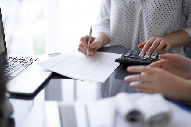 Vrouw accountant met behulp van een rekenmachine en laptopcomputer tijdens het tellen en bespreken van belastingen met een klant. Concepten voor bedrijfsaudit