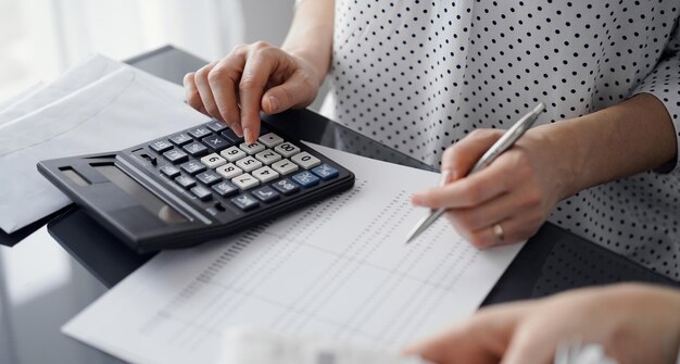 Vrouw accountant met behulp van een rekenmachine en laptopcomputer tijdens het tellen van belastingen voor een klant. Business audit en financiële concepten.
