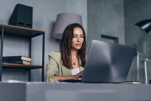 Vrouw achter haar bureau met een laptop die vanuit haar kantoor werkt.