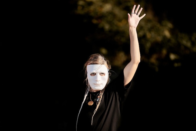 Vrouw acteert in toneelpersonage in theatermasker op gezicht openluchtpodiumkunstuitvoering Meisje theateractrice in totale zwarte stijl maakt vloeiende bewegingen in toneelrol Theatervoorstelling festival