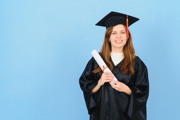 Vrouw afgestudeerde student met afstuderen hoed en jurk, op blauwe achtergrond