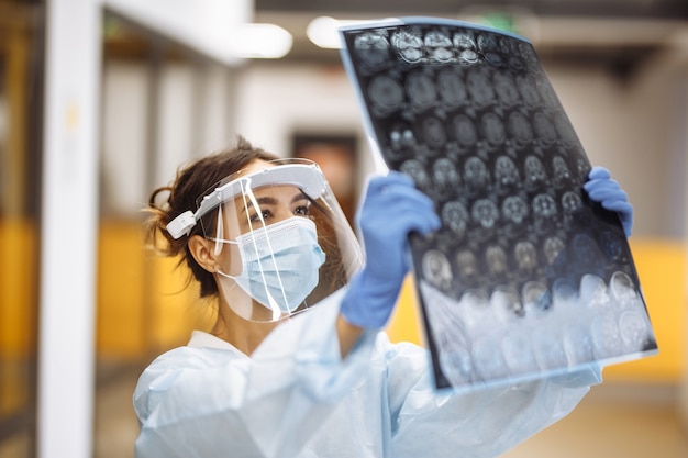 Vrouw arts controleert MRI x-ray beeld van de hersenen van de patiënt in het ziekenhuis. Vrouwelijke medische werker die beschermend masker en witte jurk draagt op de gang van een ziekenhuis. Heath en geneeskunde concept.