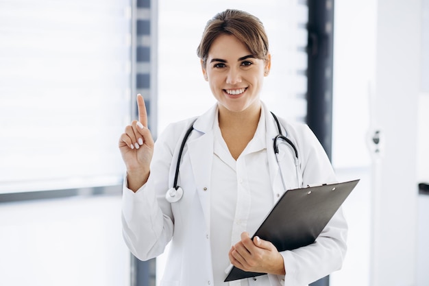 Vrouw arts in laboratoriumjas met stethoscoop wijzend met vinger