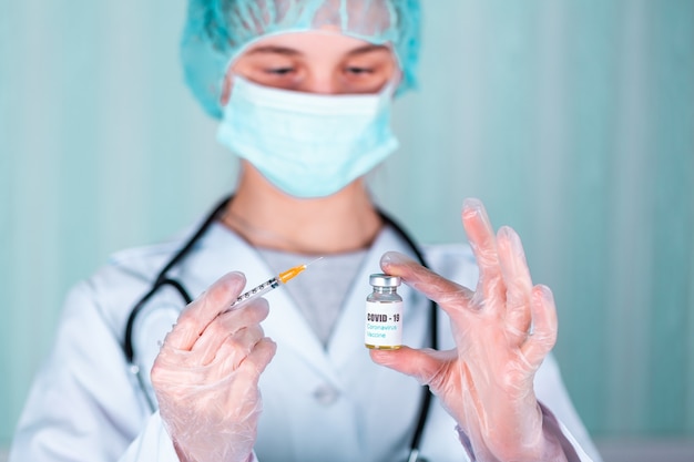 Vrouw arts of verpleegster in uniform en handschoenen met gezichtsmasker beschermend in laboratorium, met medicijnflesje vaccinfles met covid-19 coronovirus-vaccinetiket