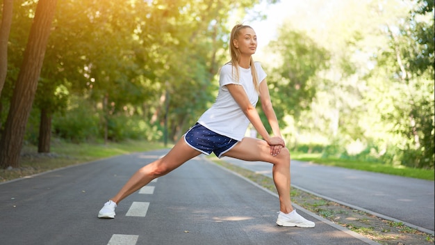 Vrouw atleet benen strekken voordat u de ochtend van het zomerpark uitoefent