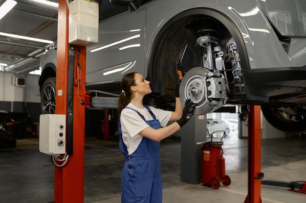 Vrouw automonteur vaststelling wielnaaf of schijfrem van verhoogde auto op liftmechanisme met behulp van moersleutel. Werk bij garageservice