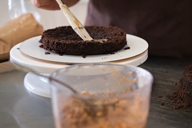 Vrouw banketbakker impregneert chocoladebiscuit op standclose-up taartbereidingsproces selectieve focus