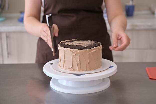 Vrouw banketbakker lijnen chocoladeroom op chocoladetaart close-up Taart maken proces Selectieve focus