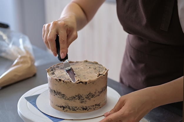 Vrouw banketbakker lijnen chocoladeroom op chocoladetaart close-up Taart maken proces Selectieve focus