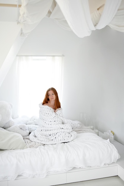 Vrouw bedekt met een dikke warme deken op het bed. Witte binnenkant. Koude winter. Elektriciteit besparen