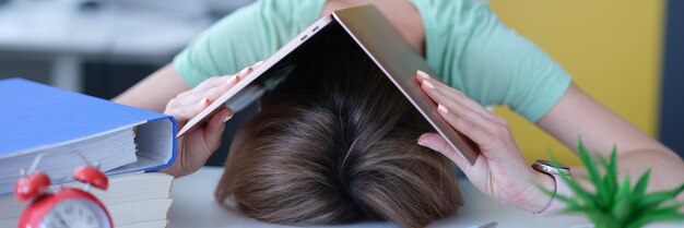 Vrouw bedekte haar hoofd met laptop en legde het op tafel op de werkplek