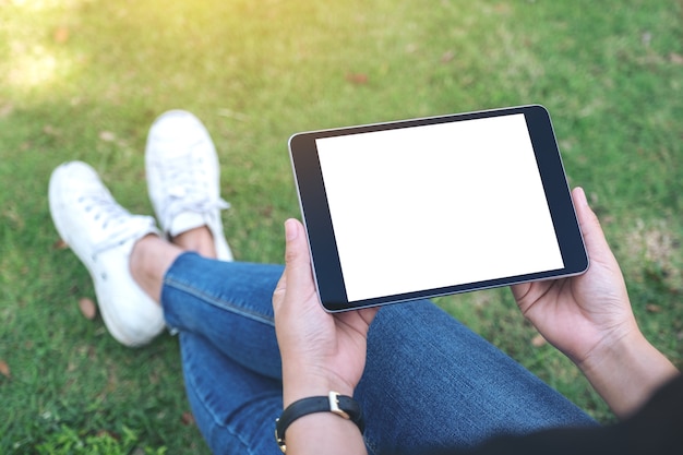 vrouw bedrijf en met behulp van zwarte tablet-pc met leeg wit scherm horizontaal zittend in het park