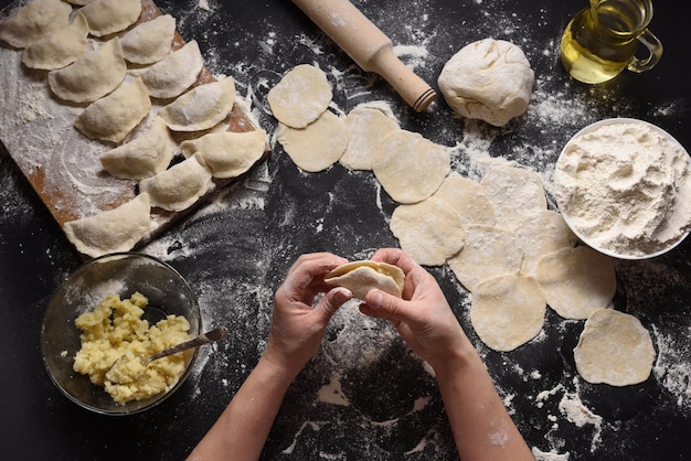 Vrouw beeldhouwt dumplings met handgemaakte aardappelen op een zwarte achtergrond Geschoten vanuit de Oekraïense volkskeuken