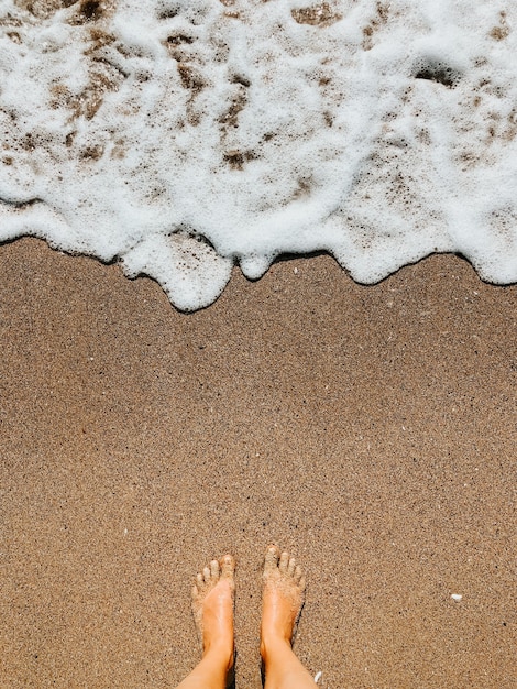 vrouw benen blootsvoets op zee schuim golven op zand strand zomerdag. bovenaanzicht boven vrouwen voeten