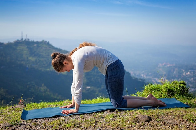 Vrouw beoefent yoga asana Marjariasana buitenshuis