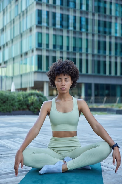 vrouw beoefent yoga in de stad mediteert en ademt diep voor stressverlichting poses in lotushouding op rubberen mat draagt sportkleding verbetert innerlijke balans serene toestand