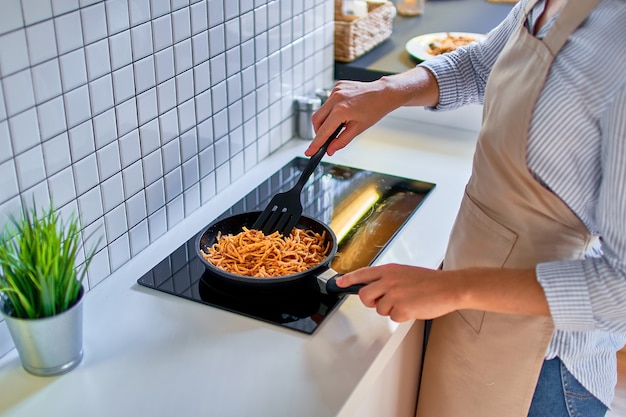 Vrouw bereiden van voedsel in een koekenpan op het fornuis voor het diner in moderne loft-stijl keuken