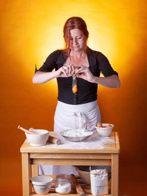 Foto vrouw bereidt eten met ei terwijl ze tegen oranje achtergrond staat