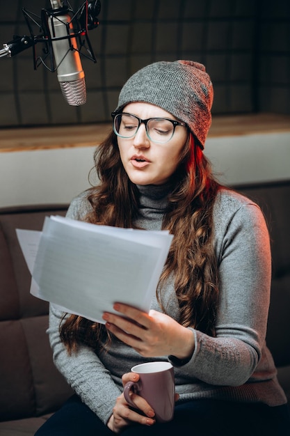 Vrouw bereidt materiaal voor vóór opname in de studio van een radioshow Geluiddichte ruimte voor professionele opname van zang Stemkunstenaar werkt met materiaal van een uitgezonden liveshow Dubbing