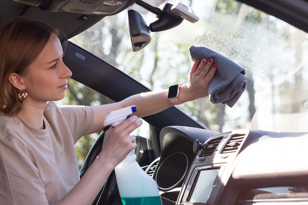 Vrouw bestuurder auto voorruit met spray reinigen, veegt met microfiber van stof en vuil.