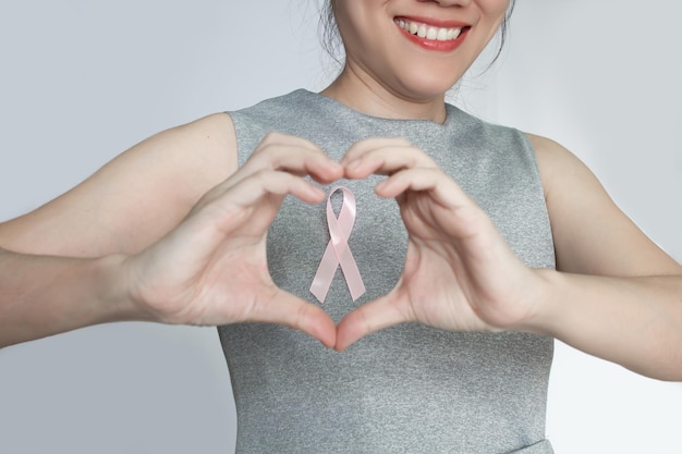 Vrouw bevestigt roze lintstrik op borst en maakt hartgebaar voor borst om borstkankerpatiënt aan te moedigen borstkankercampagne in oktobermaand