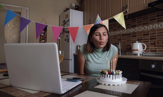 Vrouw blaast de kaars op de verjaardagstaart uit en maakt een videogesprek