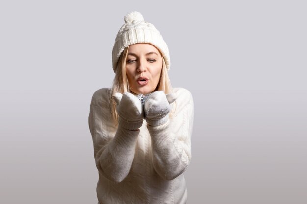 Foto vrouw blaast op sneeuwvlokken in haar handen gekleed in handschoenen hoed en trui