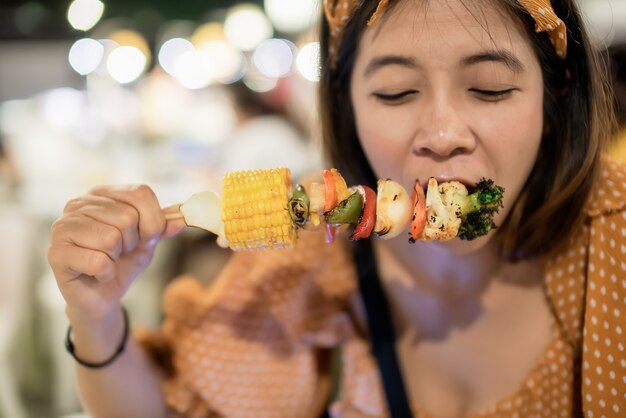 Vrouw blij en heerlijk om barbecue mager varkensvlees te eten met maïs groenten