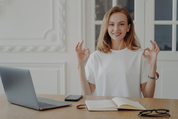 Vrouw blijft kalm en oefent yoga aan het bureau op de laptop op de werkplek Antistresspauze