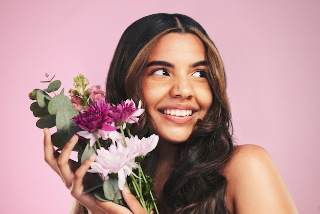 Vrouw bloemen en boeket in studio voor huidverzorging cosmetica en natuurlijke esthetiek op roze achtergrond Gezicht gelukkig model en denken aan eco schoonheid met bloemenplanten duurzaamheid en dermatologie