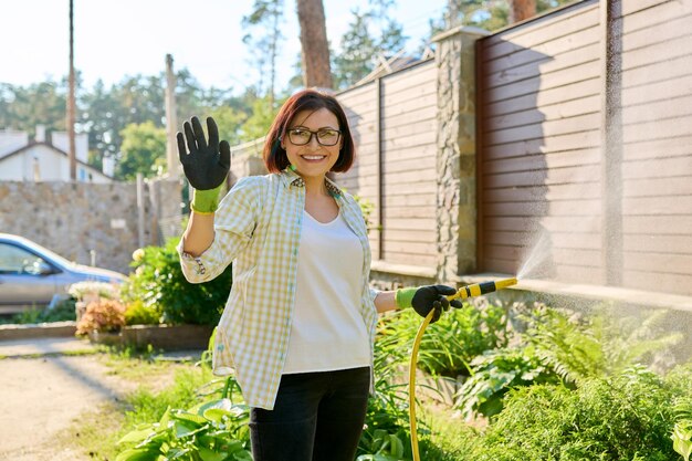 Vrouw bloemperken water geven met een slang in de tuin