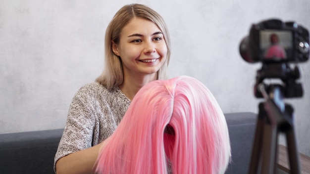 Vrouw blogger neemt video op. Ze praat over kapsels en laat een roze pruik zien. Stylist en modeadviseur die de lezing opnemen