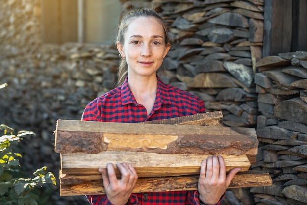 Vrouw brengt hout in handen van een houtstapel voor een open haard in huis Houtgestookte verwarming en de energiecrisis