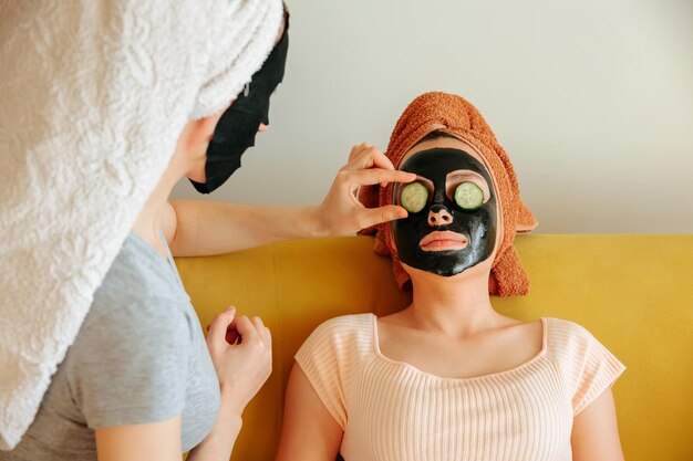 Vrouw brengt plakjes komkommer aan op het masker van haar vrienden voor cosmetische procedures voor huidverzorging