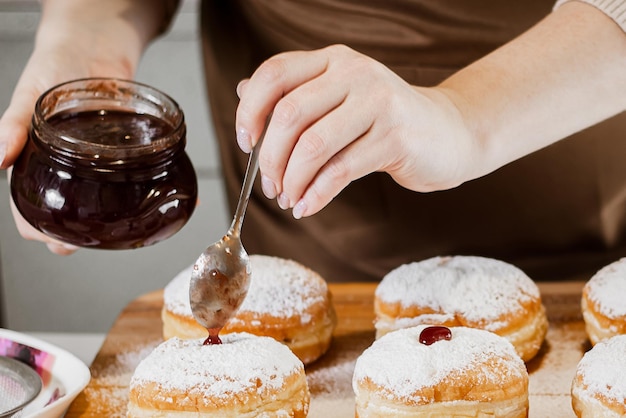 Vrouw chef-kok bereidt verse donuts met jam in haar bakkerij Koken traditionele Hanukkah sufganiyot Kleine bedrijven