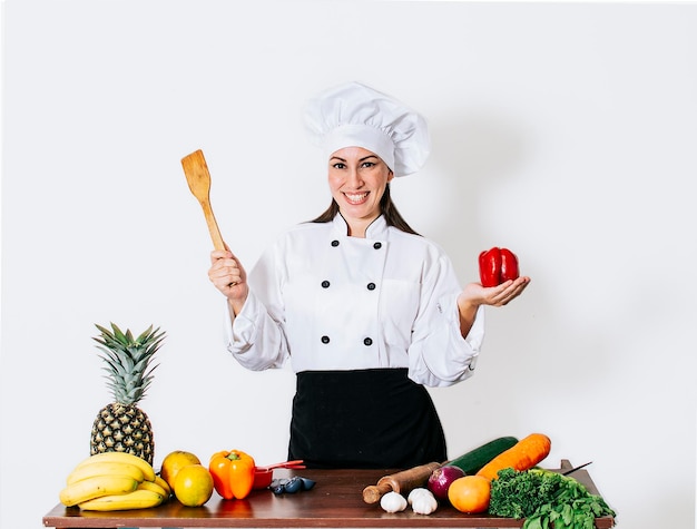 Vrouw chef-kok met een pollepel op een tafel met groenten Een lachende vrouw chef-kok met een pollepel en groenten portret van een vrouwelijke chef-kok met een pollepel op geïsoleerde achtergrond